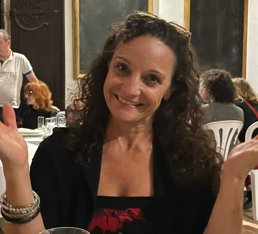 Woman smiling at a social gathering with people and tables in the background