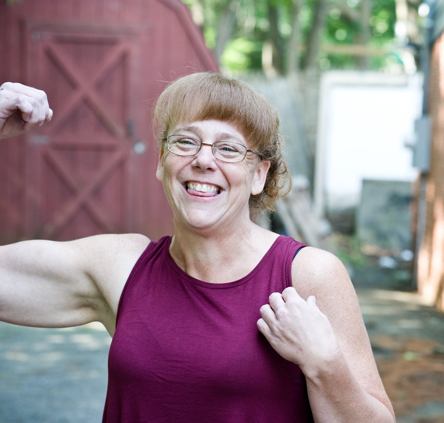Person flexing muscles outdoors with a building and trees in the background