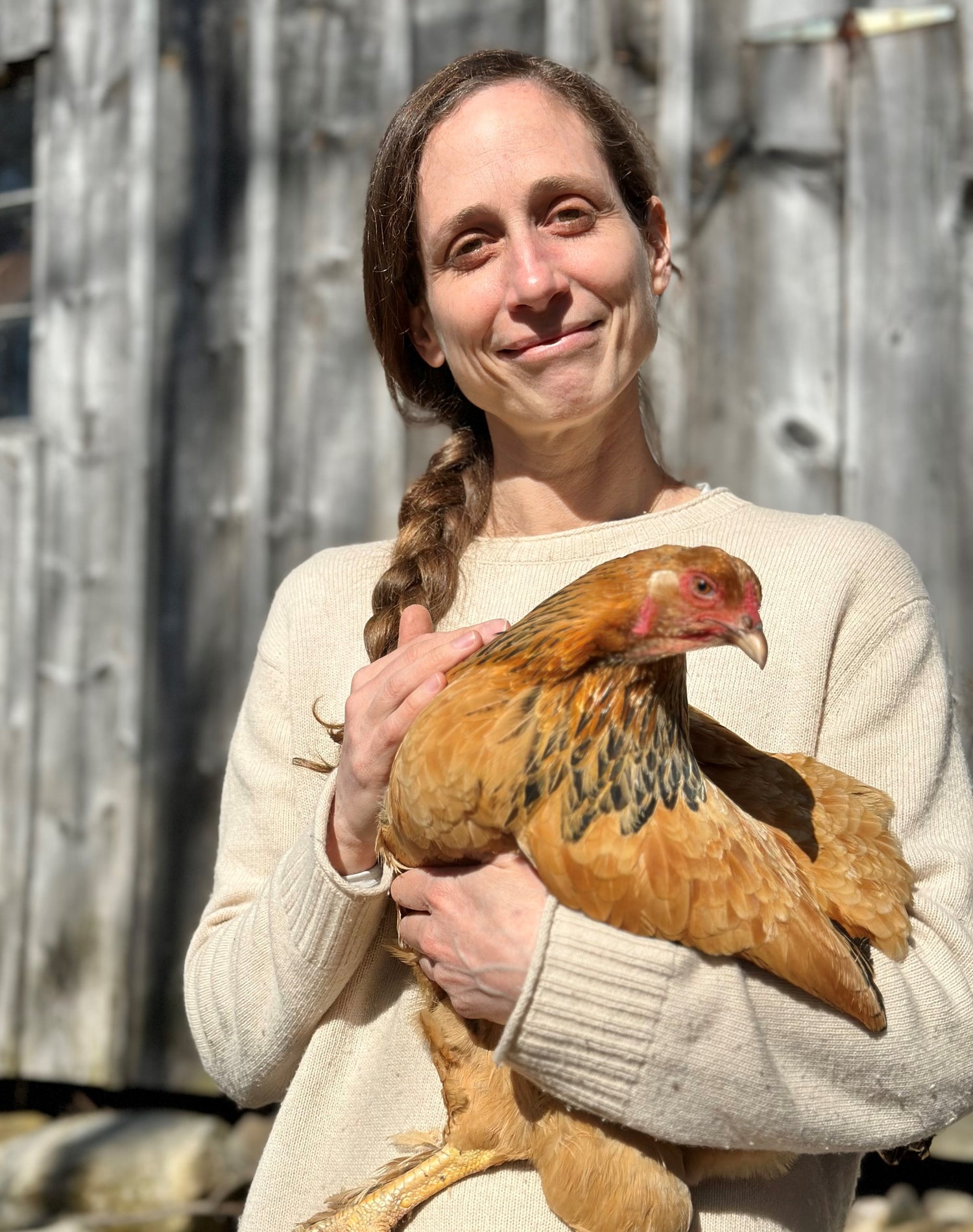 Woman holding a chicken outdoors with wooden fence in the background