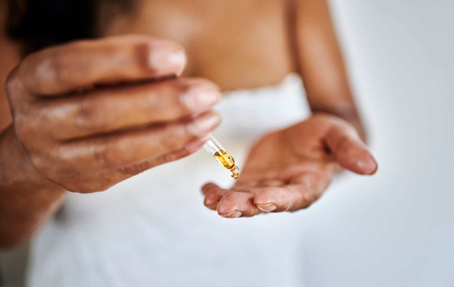 Close-up of a person applying a dropper of oil to their palm.